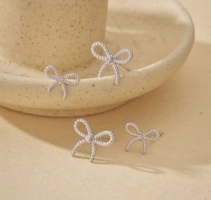 Detail of 925 sterling silver twist bow earrings set on a minimalist ceramic surface