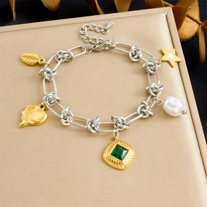 Macro view of gold-plated charms featuring green gemstone and white pearl on heart bracelet