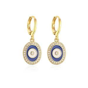 Macro detail of gold huggie hoop earring with blue enamel evil eye and zircons