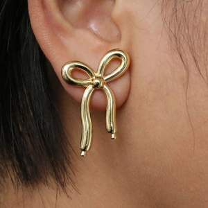 Elegant 18K gold plated brass bow ribbon stud earrings shown on a model for scale