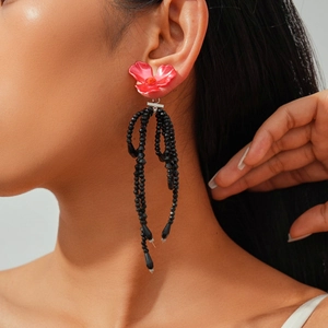 Detail of flower tassel earring with red petals and black beaded drop on model