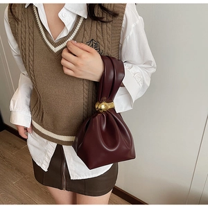 Detail view of burgundy pleated bucket bag with gold knotted metal hardware on a model