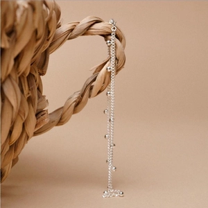 Close-up of a minimalist S925 sterling silver bead chain anklet on a woven straw background