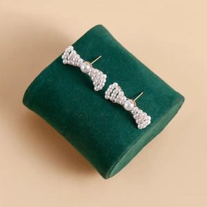 Detailed macro view of handmade woven pearl bow earrings on a dark green velvet stand