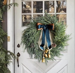 Detail of Christmas wreath with pine branches, blue ribbon bow and golden bells on a white door