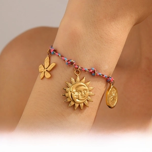Detail of woven boho bracelet with gold floral and sun pendants on a model's wrist
