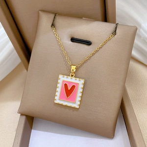 Macro view of square gold necklace with red heart pendant and crystal accents in box