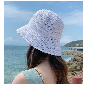 Detail of white straw sun hat with hollow weave pattern against a seaside backdrop