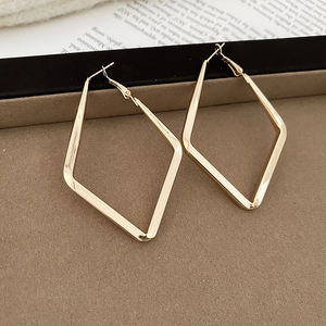 Macro shot of large golden geometric rhombus earrings on a dark velvet display tray
