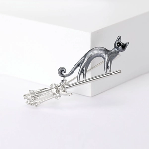 Chic grey metal cat on silver broomstick brooch with crystal accents on white background