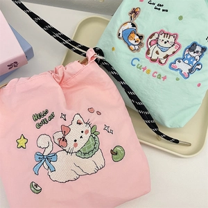 Detailed close-up of cute cat embroidery on pink and green nylon drawstring bucket bags