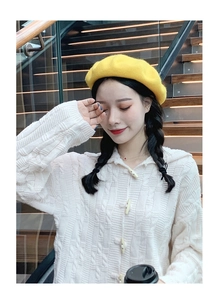 Detail showing white cable knit texture with toggle buttons and a bright yellow beret