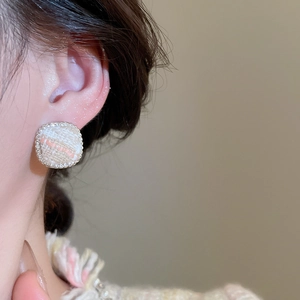 Close-up of elegant tweed fabric stud earring with sparkling rhinestone border on model