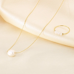 Detailed view of a gold pearl necklace and ring set on an elegant yellow silk background