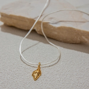 Golden conch shell pendant necklace with white cord on a textured stone background