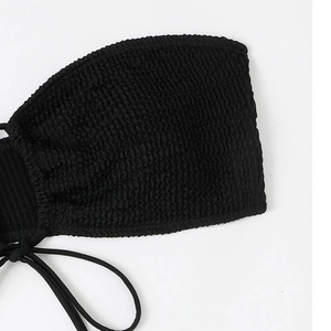 Detail view of black smocked bikini top featuring crinkled texture and side tie straps