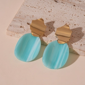 Détail de boucles d'oreilles géométriques en métal doré et pendentif en acrylique marbré bleu