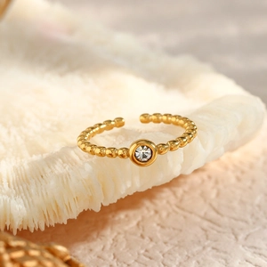 Detailed shot of gold-plated beaded open ring with a sparkling round zircon on coral