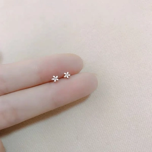 Detailed close-up showing miniature silver floral stud earrings against fingertips for scale
