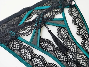 Dettaglio ravvicinato di perizoma in raso verde scuro con pizzo floreale e nappe decorative