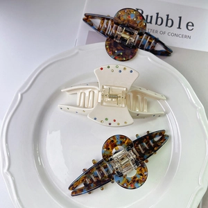 Elegant cellulose acetate hair claws with colorful rhinestones on a white ceramic plate