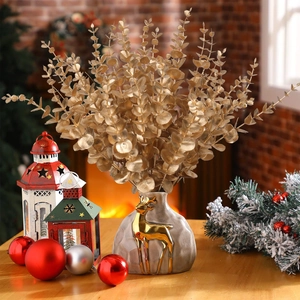Golden artificial eucalyptus stems in a ceramic vase with deer decor by the fireplace