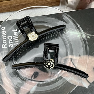 Detailed view of glossy black camellia hair claw clip on a decorative glass plate