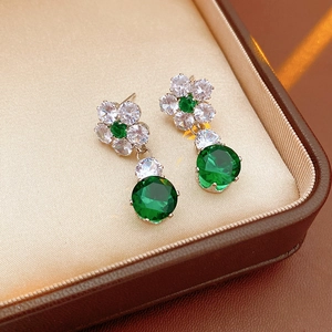 Detailed macro of gold flower earrings with green emerald gems and zircon accents