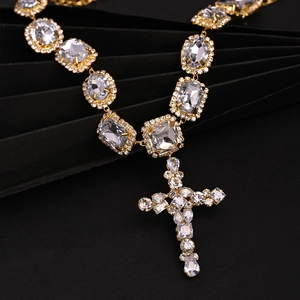 Luxury gold cross pendant necklace with sparkling white crystals on a black textured background