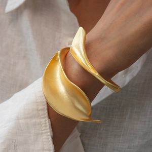 Detailed view of matte gold leaf cuff bracelet with organic fluid curves on a linen sleeve