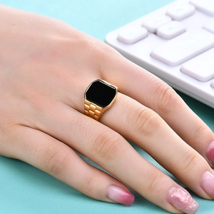 Detail of gold watchband style stainless steel ring with square black stone on finger