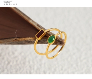 Detail of minimalist gold-plated rings with red baguette and green oval stones