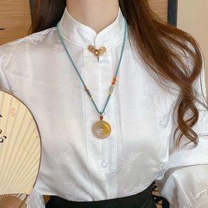 Detail of emerald Ping'an buckle necklace with blue braided cord on silk clothing