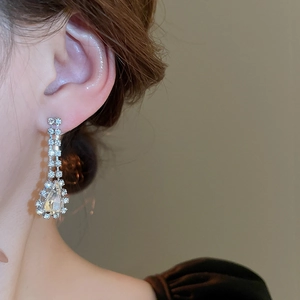 Close-up of silver tassel earrings with tiered rhinestones worn on a model's ear
