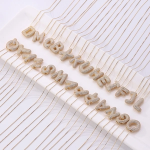 Multiple gold-plated necklaces with zircon-encrusted alphabet pendants on a white display