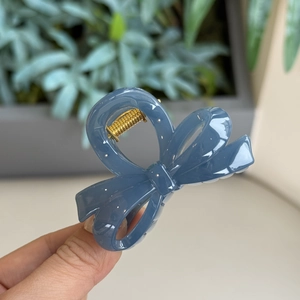 Macro detail of the grey-blue resin bow hair claw clip with a strong gold metal spring