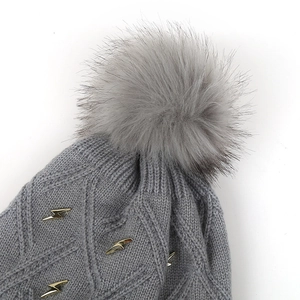 Detailed macro view of gray knitted beanie with large faux fur pom and golden lightning charms