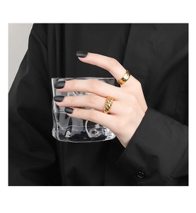 Detail of gold croissant ring and wide band ring on model holding a glass cup