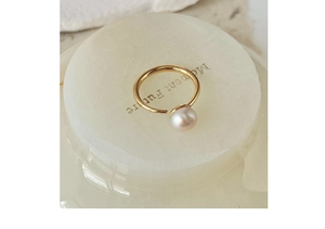 Detailed close-up of a gold open ring with a white pearl on a decorative white stand