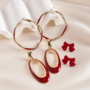Set of gold earrings with wine red oval drops and red bow studs on silk fabric