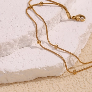 Detailed macro view of gold plated 18K double layer bead snake chain anklet on stone
