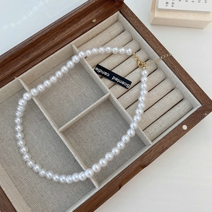 Detailed view of elegant white pearl necklace with golden lobster clasp in a wooden box