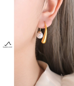 Detail of gold stainless steel curved earring with white pearl on model