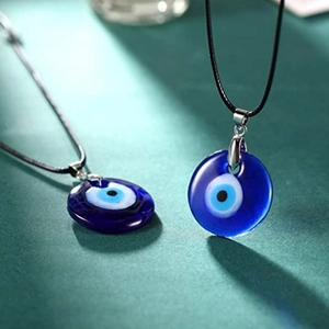 Vue détaillée de pendentifs œil bleu en verre sur cordon noir avec fond texturé vert