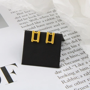 Close-up of golden rectangular hollow earrings on a black display card and book page