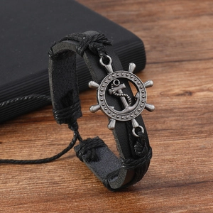 Detail of woven black leather bracelet with vintage metal rudder charm on wooden desk