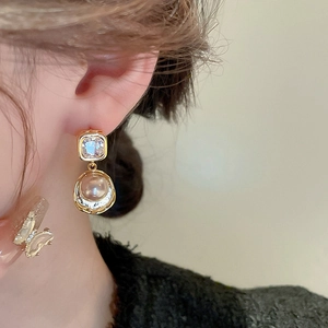 Detail view of gold plated earrings featuring square crystal and round pearl on a model