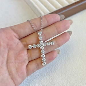 Detail of silver cross pendant with heart-shaped cubic zirconia held in hand