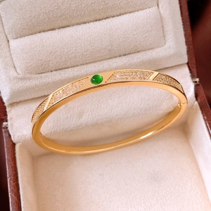 Macro detail of 18K gold-plated bangle featuring a green gemstone and pave-set zircons