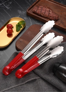 Detail of two stainless steel food tongs with red handles on a dark table cloth